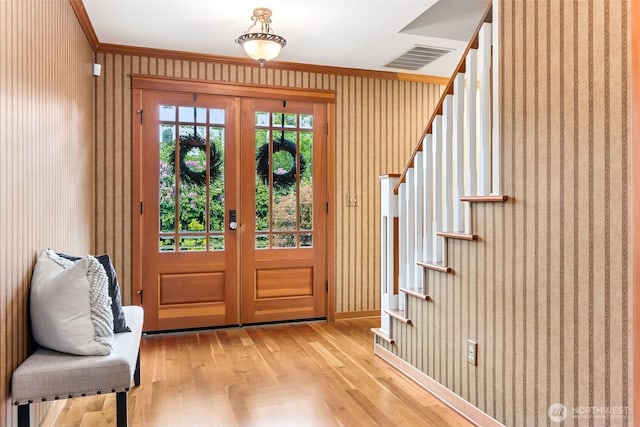 foyer featuring stairs, light wood-style floors, french doors, crown molding, and wallpapered walls