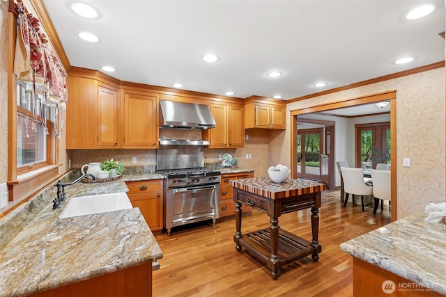 kitchen with stainless steel gas range, wall chimney exhaust hood, a sink, ornamental molding, and wallpapered walls