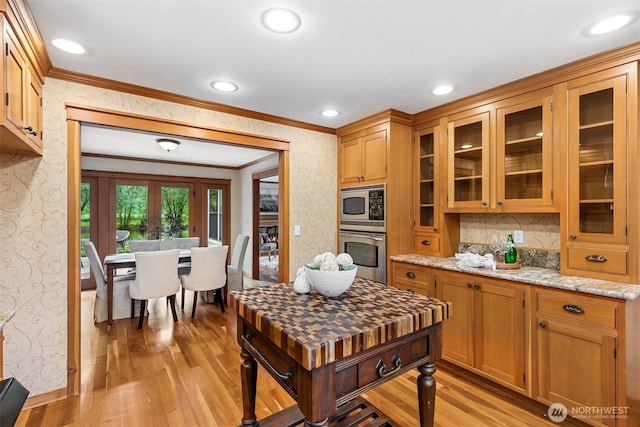kitchen featuring stainless steel appliances, wallpapered walls, crown molding, light wood finished floors, and glass insert cabinets