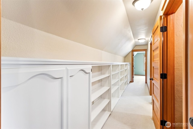 hall with vaulted ceiling, light carpet, and a textured wall