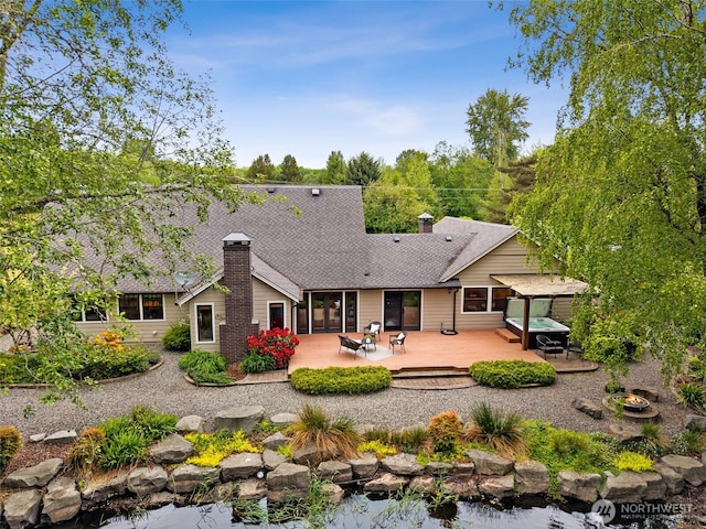 rear view of property with a deck, a chimney, and roof with shingles