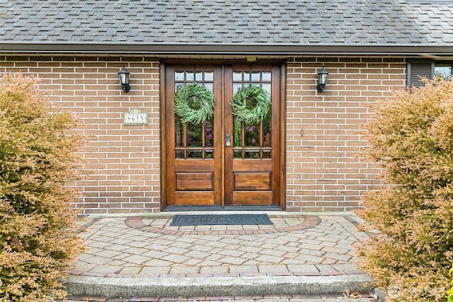 entrance to property with french doors, roof with shingles, and brick siding