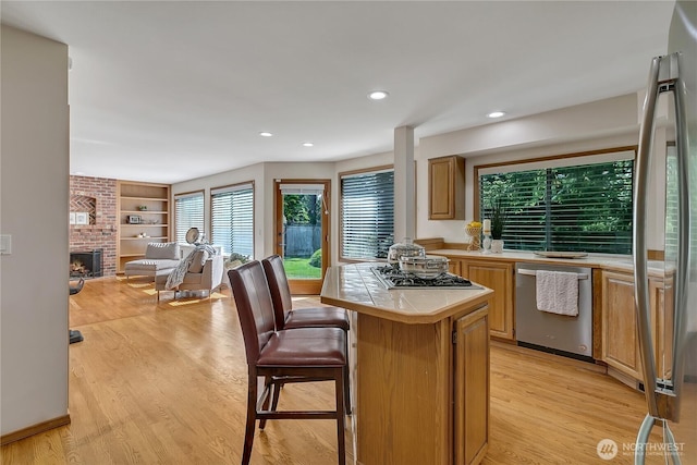 8612 165th Street Ct E, Puyallup, WA 98375 - kitchen featuring appliances with stainless steel finishes, tile countertops, light wood-style floors, a brick fireplace, and a breakfast bar