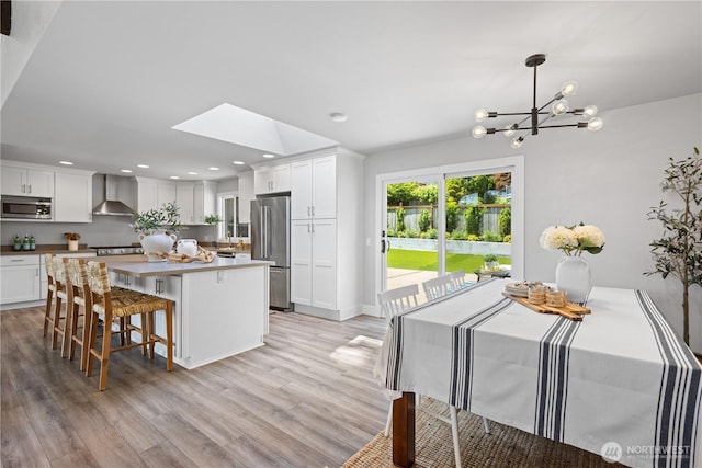 17905 NE 19th Pl, Bellevue, WA 98008 - kitchen with appliances with stainless steel finishes, wall chimney range hood, a chandelier, a kitchen island, and light wood-style flooring