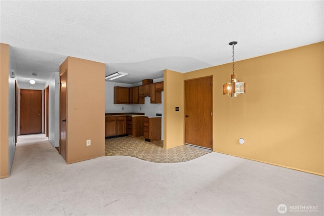 kitchen featuring brown cabinets, pendant lighting, open floor plan, a textured ceiling, and a chandelier