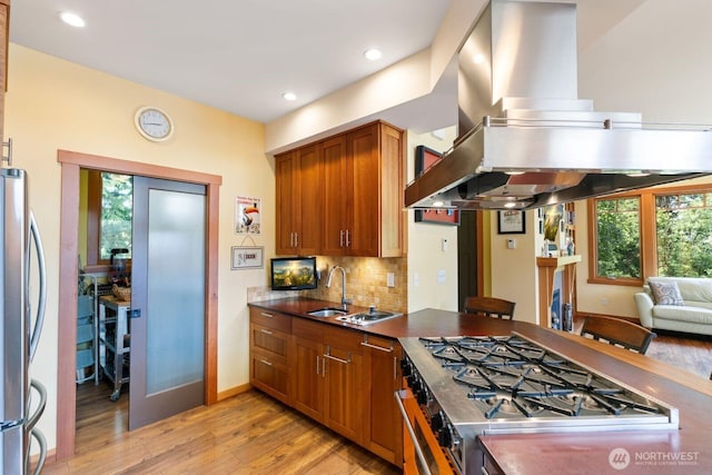 1433 Madison St, Port Townsend, WA 98368 - kitchen with island range hood, appliances with stainless steel finishes, light wood-style floors, brown cabinetry, and backsplash