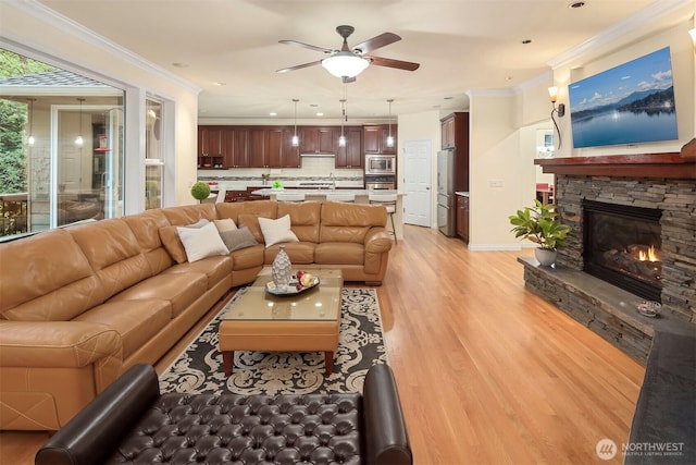 living room with light wood-type flooring, a ceiling fan, a fireplace, crown molding, and recessed lighting