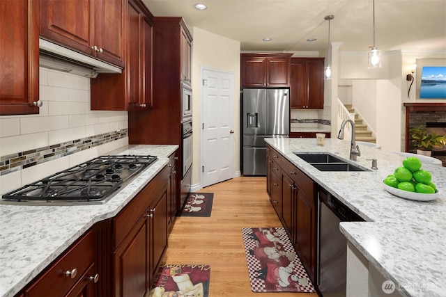kitchen with appliances with stainless steel finishes, a sink, pendant lighting, light wood-style floors, and under cabinet range hood