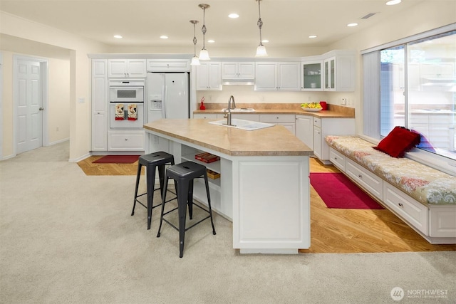 kitchen featuring white appliances, white cabinetry, light countertops, a kitchen breakfast bar, and recessed lighting