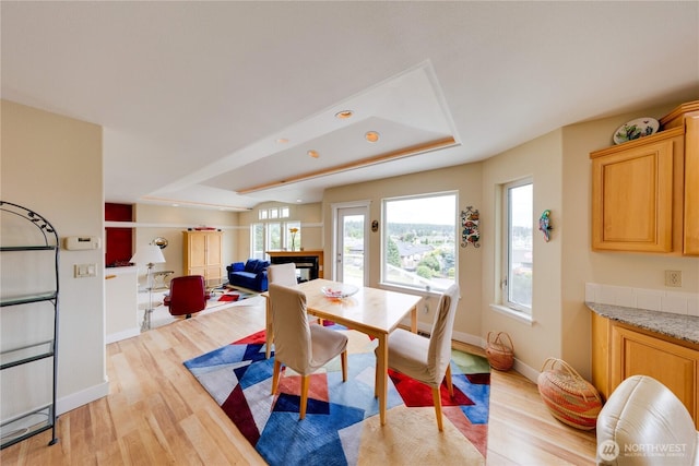 dining space featuring light wood finished floors, baseboards, and a tray ceiling