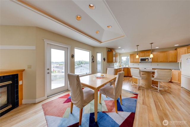 dining room with light wood-style flooring, recessed lighting, a tiled fireplace, and baseboards