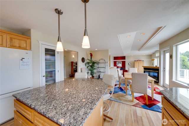 kitchen featuring freestanding refrigerator, a glass covered fireplace, light wood-type flooring, light stone counters, and a center island
