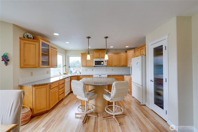 kitchen featuring white appliances, a center island, light wood-type flooring, glass insert cabinets, and recessed lighting