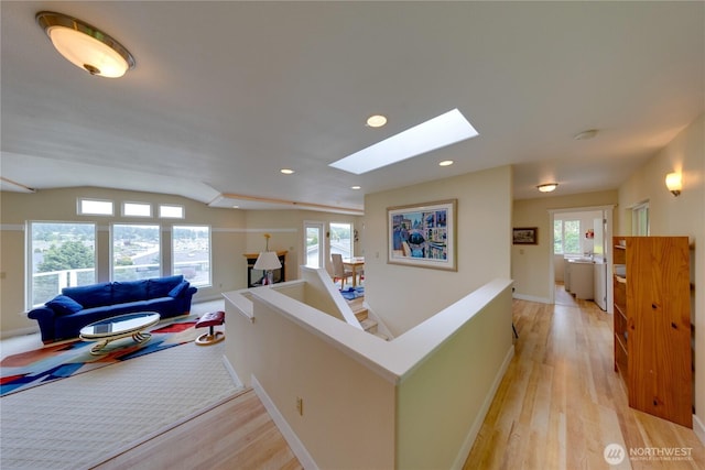 hallway featuring an upstairs landing, a skylight, light wood-style flooring, baseboards, and recessed lighting
