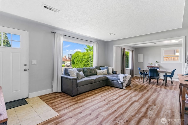 living area featuring light wood-style flooring, a textured ceiling, and baseboards