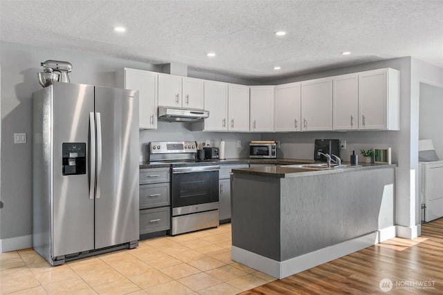 kitchen with stainless steel appliances, under cabinet range hood, a peninsula, white cabinets, and a textured ceiling