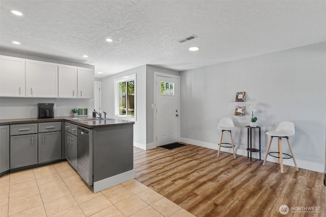 kitchen with a sink, a peninsula, dishwasher, baseboards, and gray cabinets