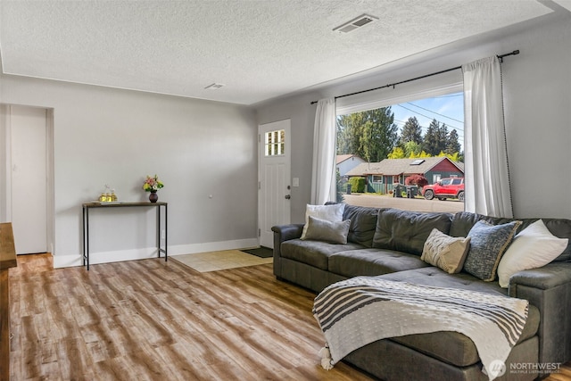 living area featuring light wood-type flooring, a textured ceiling, and baseboards