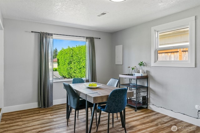 dining room with healthy amount of natural light, wood finished floors, baseboards, and a textured ceiling