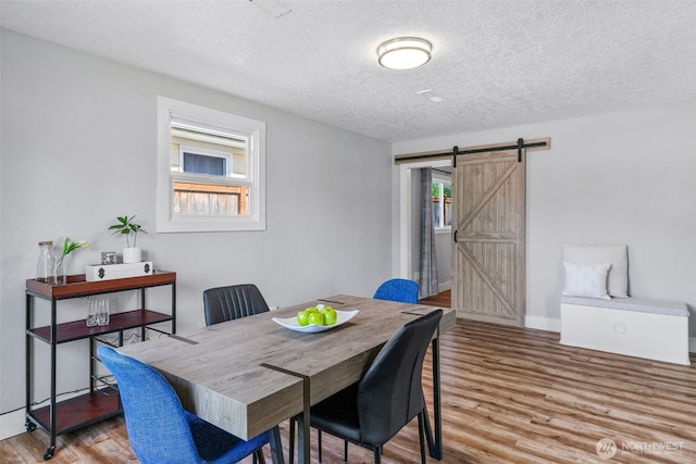 dining space with a barn door, wood finished floors, a textured ceiling, and baseboards