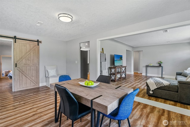 dining space featuring a barn door, wood finished floors, baseboards, and a textured ceiling
