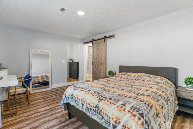 bedroom featuring wood finished floors, a barn door, a textured ceiling, baseboards, and recessed lighting