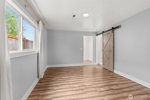 unfurnished bedroom featuring baseboards, a barn door, light wood finished floors, and recessed lighting