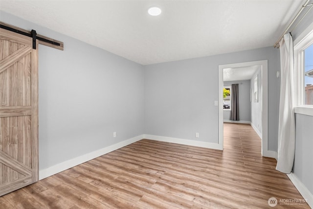 spare room featuring light wood-type flooring, baseboards, and a barn door