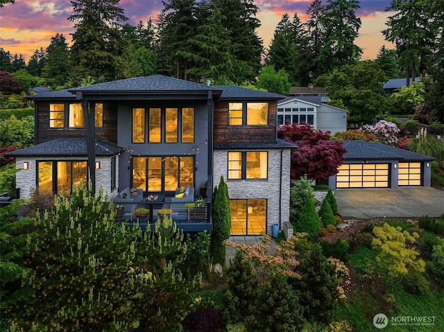 8326 84th Ave SE, Mercer Island, WA 98040 - back of house at dusk with stone siding, an outbuilding, concrete driveway, and view of scattered trees
