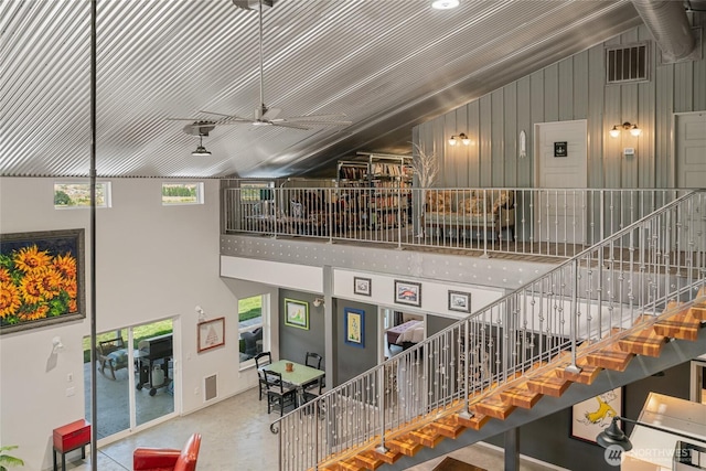 stairs with high vaulted ceiling, a ceiling fan, and concrete floors