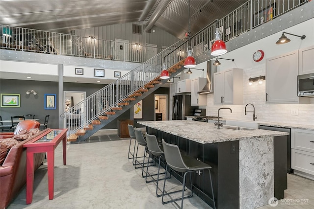 kitchen with high vaulted ceiling, a sink, concrete floors, an island with sink, and stainless steel microwave