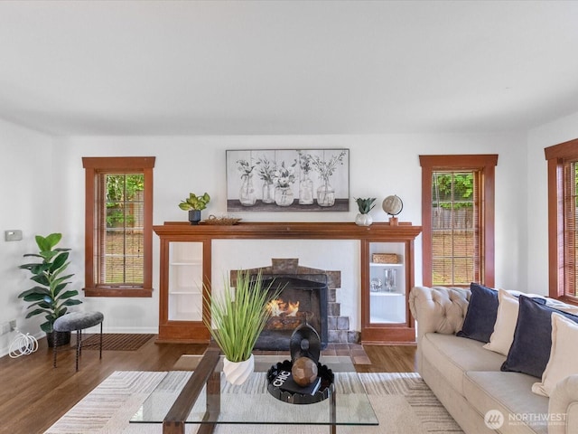 living room with wood finished floors, a fireplace with flush hearth, plenty of natural light, and baseboards