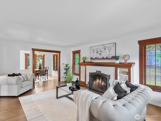 living room with a chandelier, wood finished floors, and a warm lit fireplace