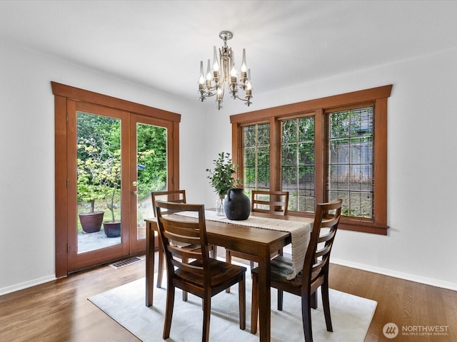 dining area with french doors, healthy amount of natural light, a chandelier, and wood finished floors
