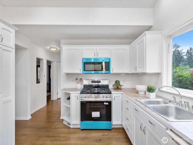 kitchen with appliances with stainless steel finishes, a sink, white cabinets, wood finished floors, and light countertops