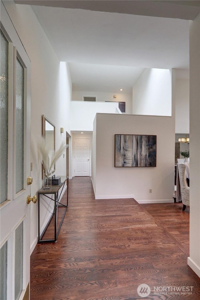 hallway featuring wood finished floors, baseboards, a high ceiling, and recessed lighting