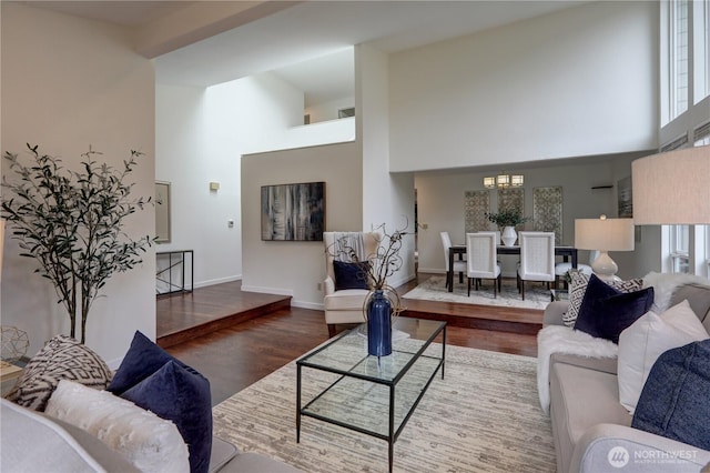 living area featuring high vaulted ceiling, wood finished floors, a chandelier, and baseboards