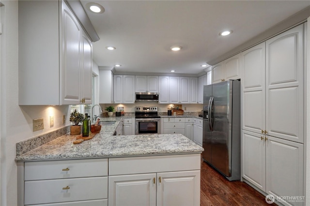 kitchen featuring stainless steel appliances, a sink, a peninsula, dark wood-style floors, and white cabinets