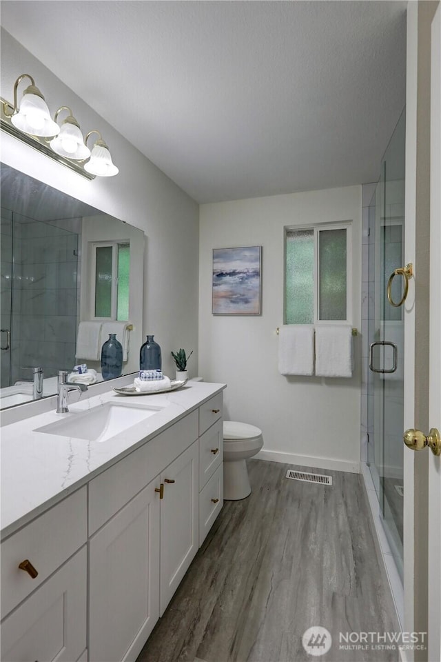 bathroom with wood finished floors, toilet, vanity, and a shower stall