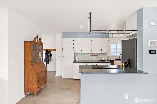 kitchen with freestanding refrigerator, dark countertops, light wood finished floors, a peninsula, and white cabinetry