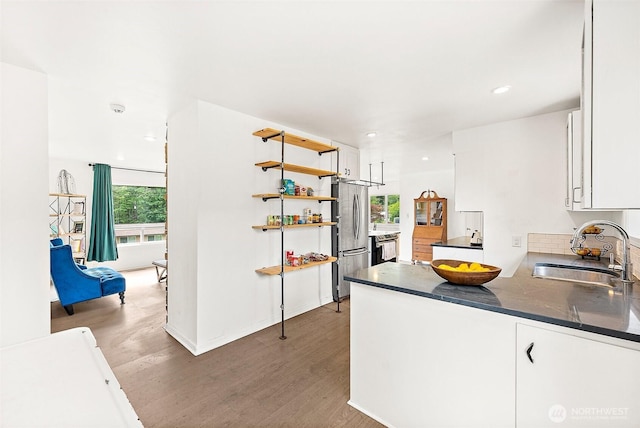 kitchen featuring a sink, wood finished floors, freestanding refrigerator, dark countertops, and recessed lighting