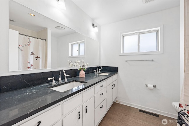 full bathroom featuring wood finished floors, toilet, double vanity, and baseboards