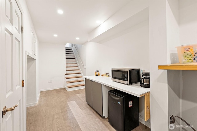 kitchen featuring stainless steel microwave, refrigerator, light wood finished floors, light countertops, and recessed lighting
