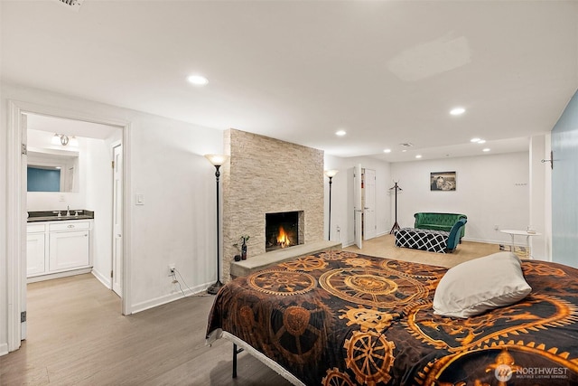 bedroom featuring light wood-style floors, baseboards, recessed lighting, a sink, and a stone fireplace