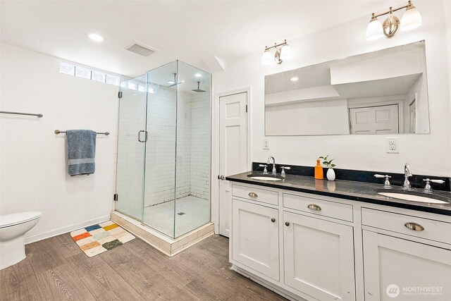 bathroom with wood finished floors, a stall shower, double vanity, and toilet