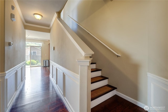 stairs featuring wainscoting, wood finished floors, a decorative wall, and ornamental molding