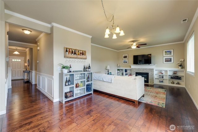 living room with a ceiling fan, dark wood-style flooring, a chandelier, a glass covered fireplace, and crown molding