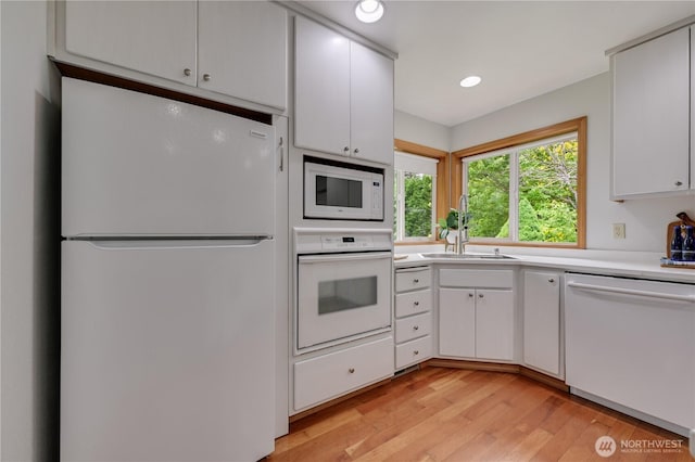 kitchen featuring white appliances, a sink, light countertops, light wood-type flooring, and white cabinetry