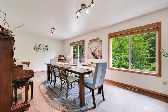 dining space with light wood-type flooring, rail lighting, and baseboards