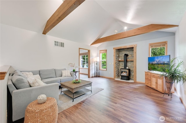 living area with a wood stove, light wood finished floors, beam ceiling, baseboards, and high vaulted ceiling